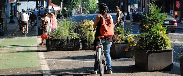 Bicyclists ride in a protected bike lane, buffered by planters